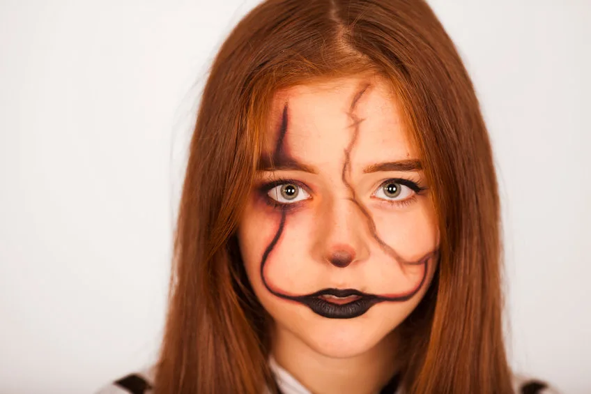 mystical girl with a painted skull on her face in the style of halloween. close up portrait of beautiful girl with fluttering hair. professional halloween makeup
